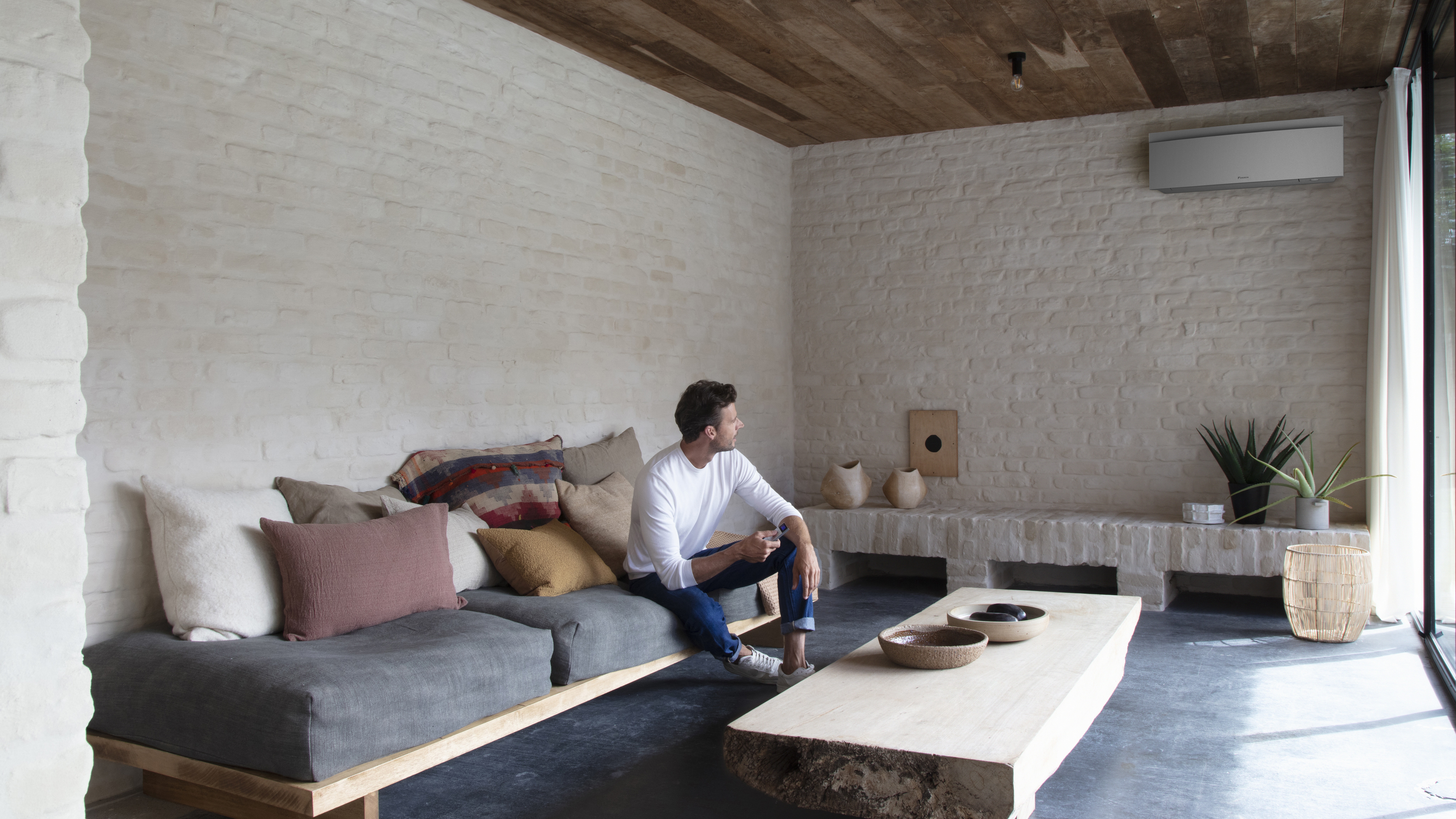 Man op zijn bank stelt de perfecte temperatuur in op deze Comfora binnenunit met afstandsbediening