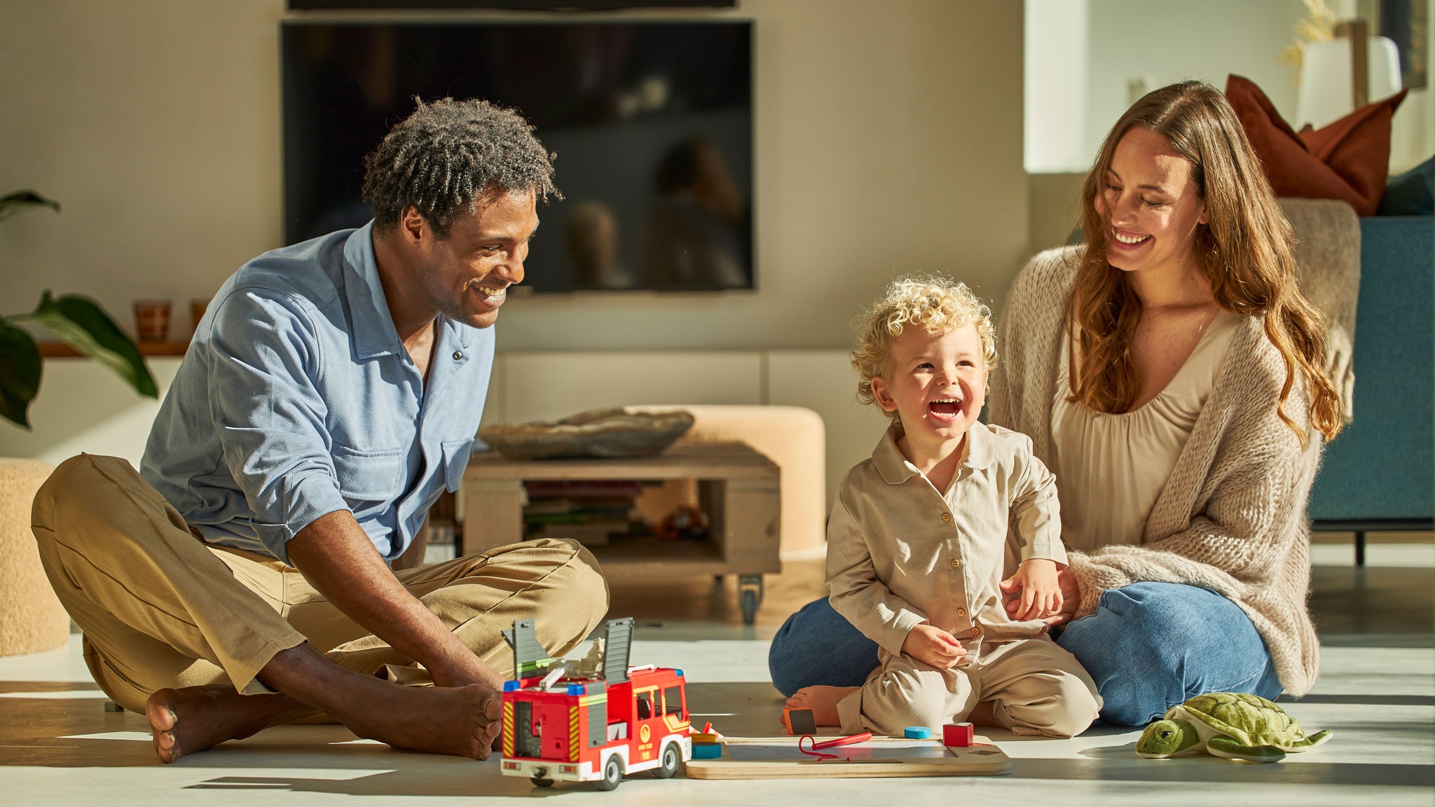 Parents et enfant en bas âge assis sur le sol et jouant avec des jouets dans un logement ventilé