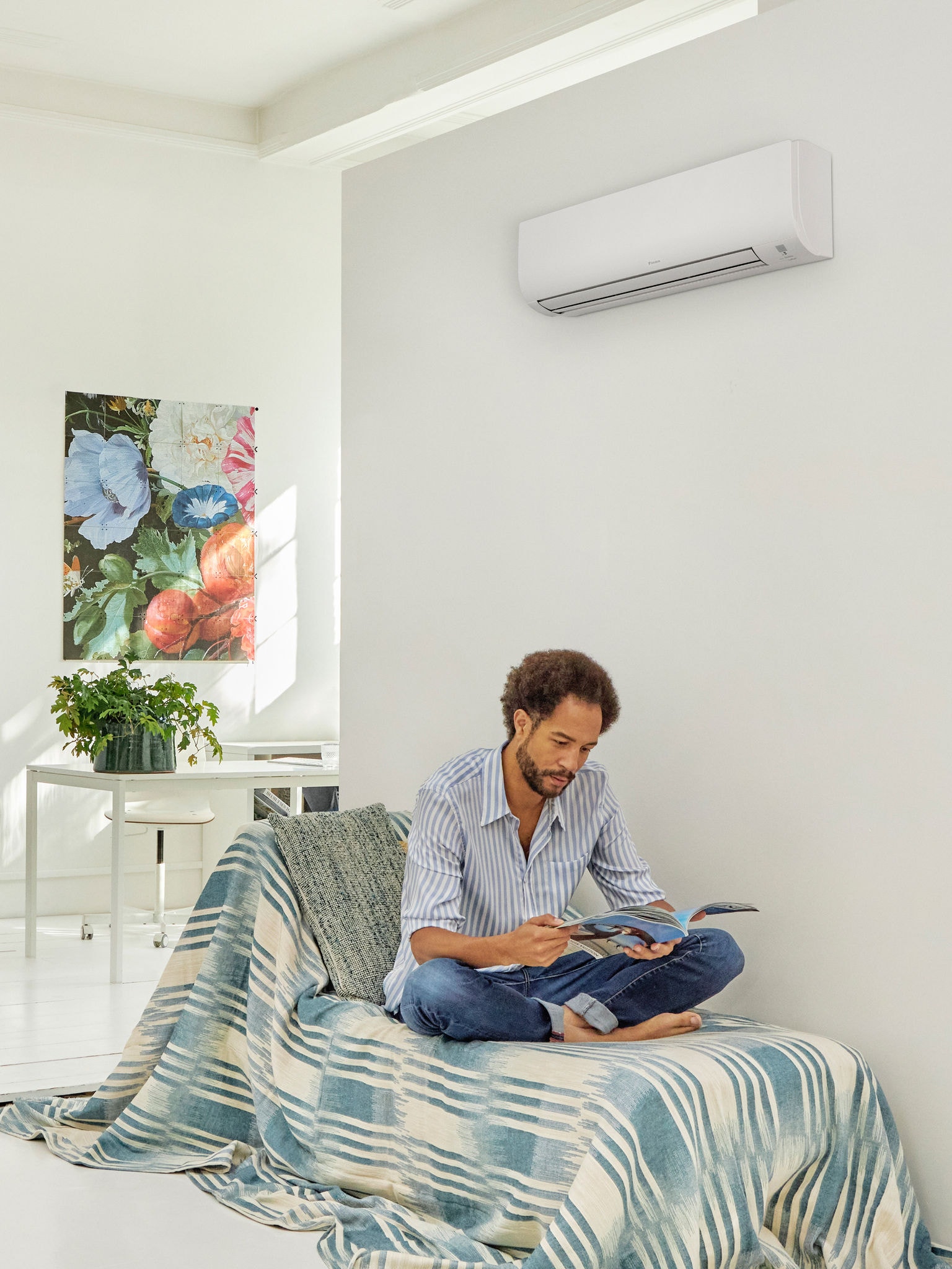 Lezende man in een lichte, moderne leefruimte met een warmtepomp aan de muur, ter illustratie van het comfort en het energierendement van warmtepomptechnologie die wordt ondersteund door overheidsmaatregelen