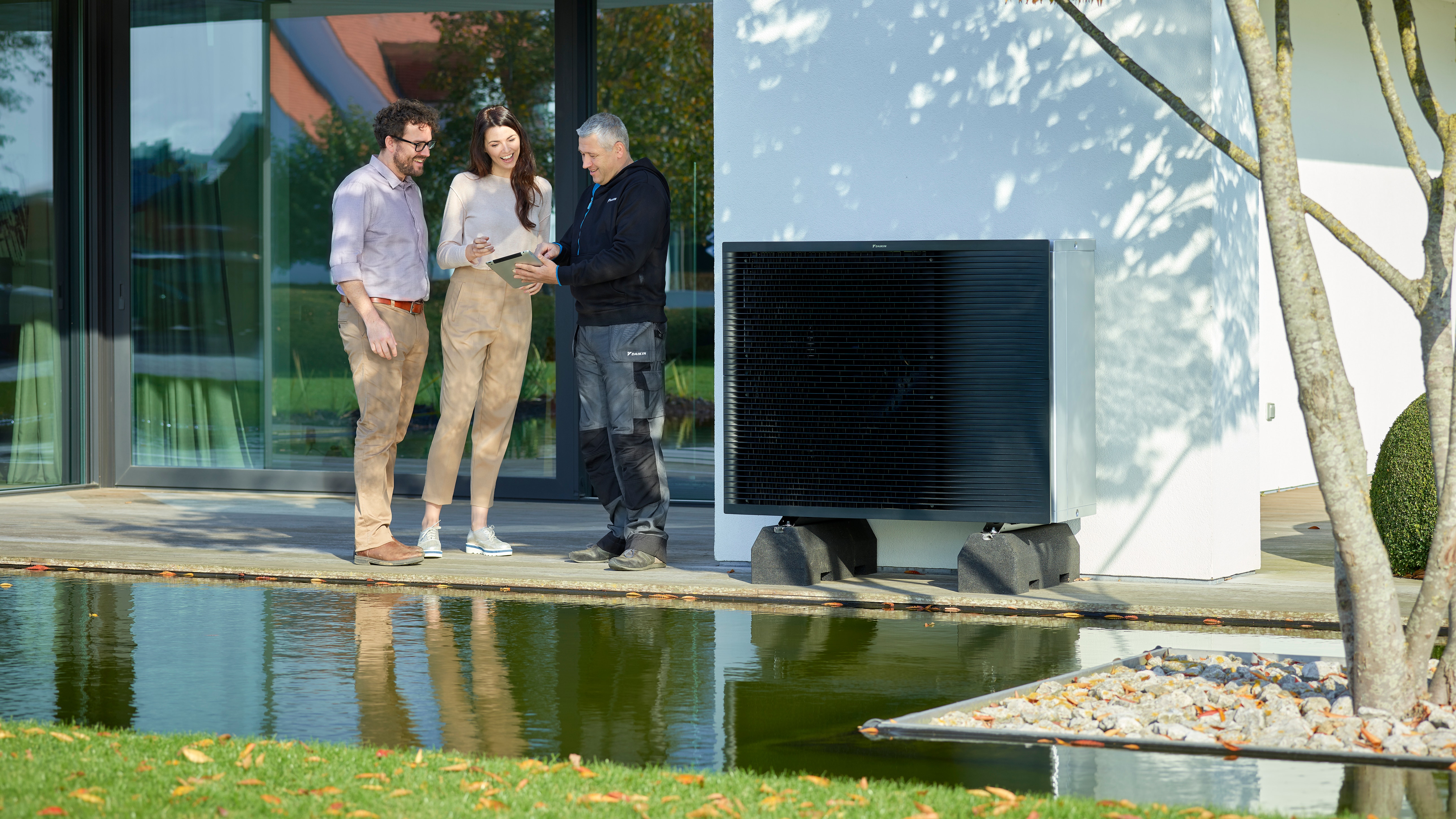 Couple discutant avec un installateur à côté du groupe extérieur d'un Daikin Alterma dans leur jardin
