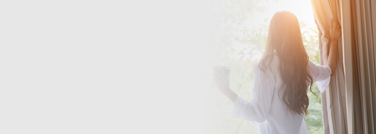 Vrouw kijkt naar buiten terwijl ze de gordijnen vasthoudt.